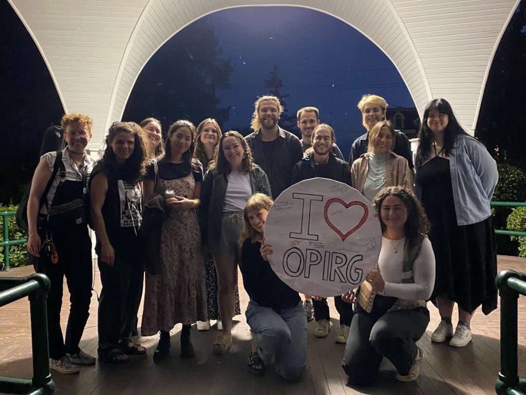 OPIRG volunteers gathered under a gazebo with a round white sign that reads "I love OPIRG"
